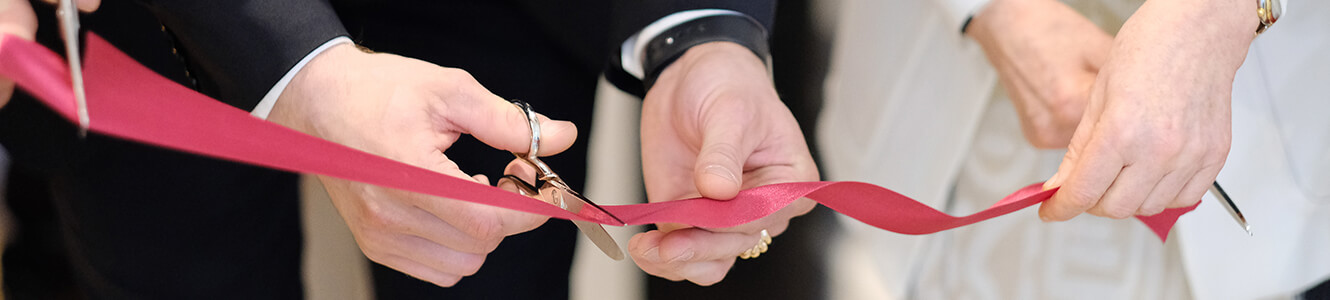 Image of two people cutting a red ribbon, in celebration of a grand opening.