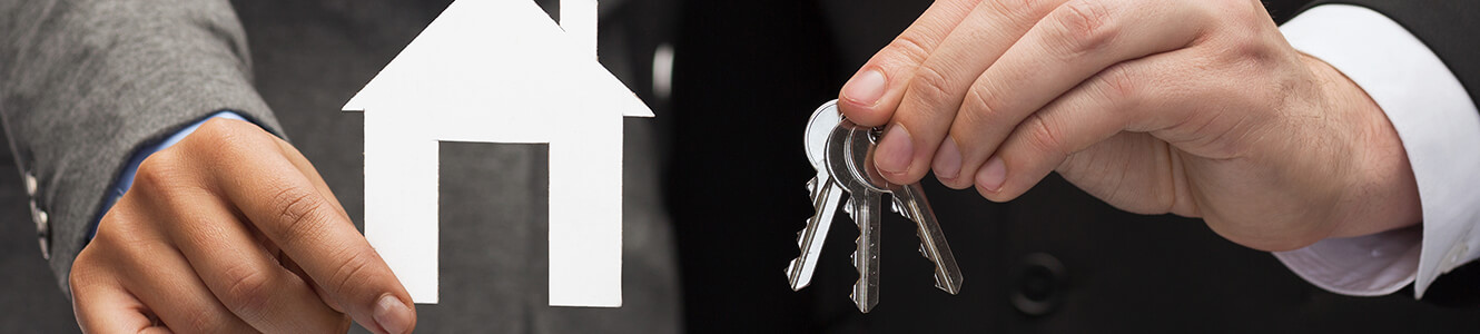 Photo of a man holding a cardboard cut out of a house and a set of keys, meant to represent purchasing a new home.