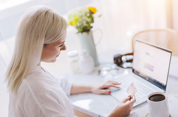 Blonde woman glancing down at her atm card as she reviews her bank account on a laptop computer.